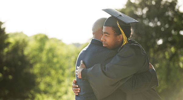 Son in a graduation gown hugging his father stock photo